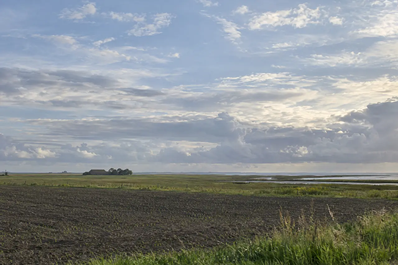 Open kleiland met een verre boerderij onder een grote lucht