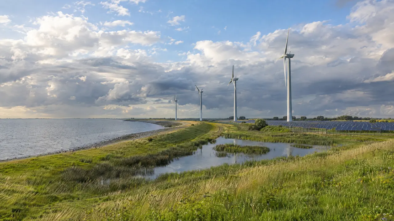 Windturbines, zonnepanelen en een waterbuffer langs een dijk